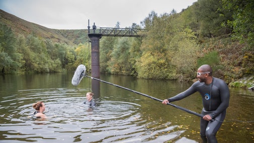 Two people swimming while a man holds a mic. boom close above them